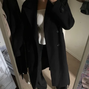 Svart kappa  - Snygg svart kappa med knappar och bälte i midjan. 