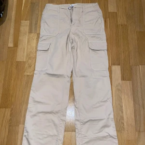 Beige cargobyxor från Zara - Säljer ett par beige cargobyxor från Zara med flera praktiska fickor och dragkedja. Byxorna har en avslappnad passform och är perfekta för en casual look. Tillverkade i ett bekvämt material som passar bra för vardagsbruk.