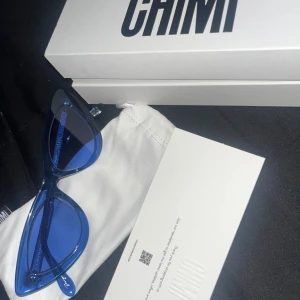 Blå solglasögon från Chimi - Snygga blå solglasögon från Chimi med en modern och stilren design. De har en kantig form och kommer med ett vitt fodral. Perfekta för att ge din outfit en färgklick.