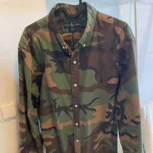 Camouflage skjorta från Ralph Lauren - Säljer en cool camouflage skjorta från Ralph Lauren. Skjortan har långa ärmar och knappar framtill. Perfekt för en avslappnad stil.