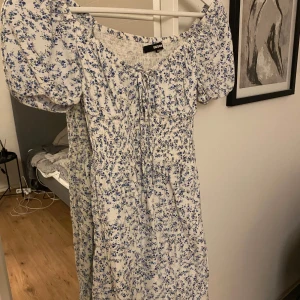 Blommig klänning från BikBok - Säljer en söt blommig klänning från BikBok i storlek S. Klänningen har korta puffärmar och ett fint blått blommönster på vit bakgrund. Den har en smockad överdel och knytning framtill 🩷Perfekt för sommarens alla tillfällen!