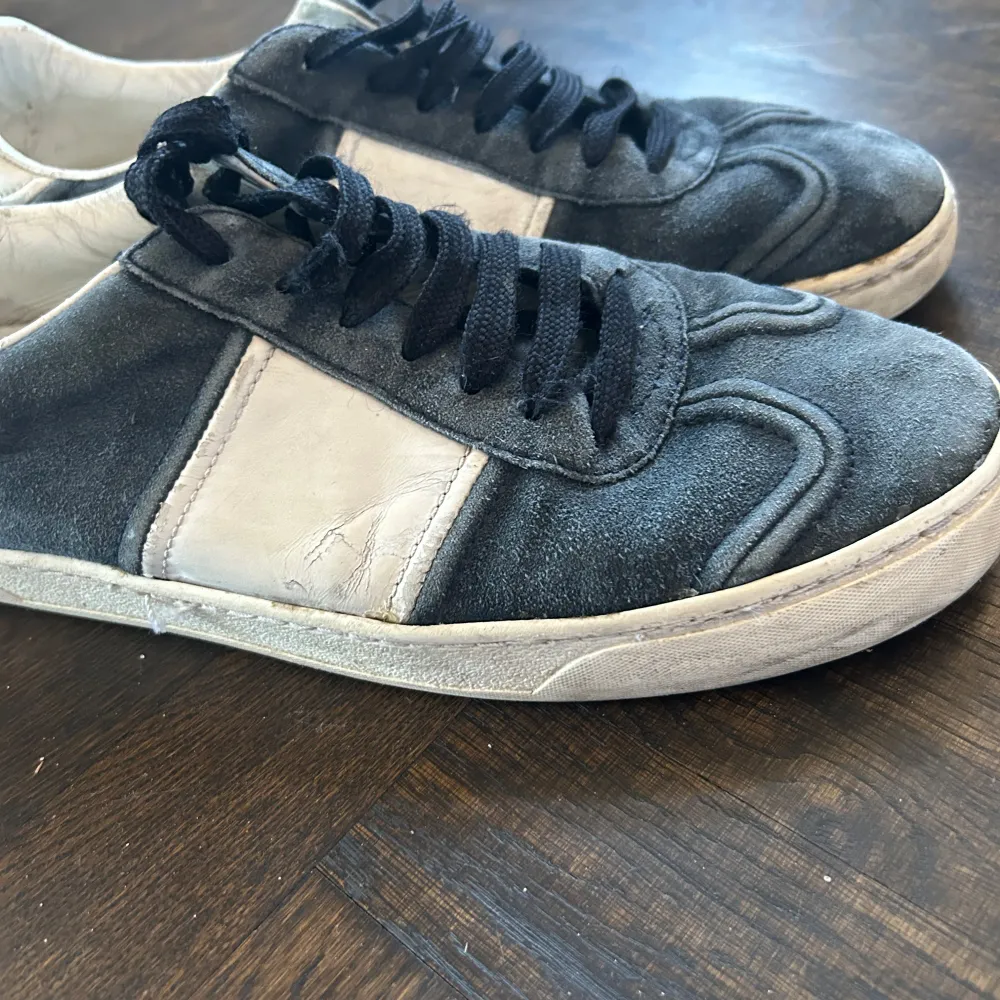 Snygga sneakers från Valentino Garavani i grå mocka med vita detaljer. Skorna har svarta snören och en rund tå. Perfekta för en stilren look med en touch av lyx, som är äkta.. Kengät.