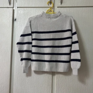 Vit och svart randig stickad tröja - Säljer en snygg vit stickad tröja med svarta ränder. Tröjan har en klassisk design med långa ärmar och ribbade muddar. Perfekt för en stilren look.