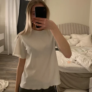 Vit ribbad t-shirt - Säljer en stilren vit ribbad t-shirt med korta ärmar. Perfekt för en avslappnad look. Passar till det mesta och är ett måste i garderoben!