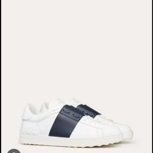 Vita sneakers med mörkblå detalj söker - Snygga vita sneakers från Valentino med en bred mörkblå rem över ovansidan. Skorna har en klassisk design söker! Skriv till mig om ni kan sälja 