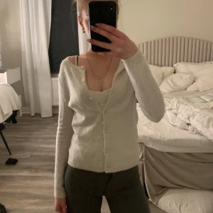 Vit kofta med knappar - Säljer en stilren vit kofta med knappar framtill. Den har en v-ringad design och långa ärmar, perfekt för lager-på-lager-stil. Passar till både vardag och mer uppklädda tillfällen. Perfekt för dig som gillar en klassisk look.