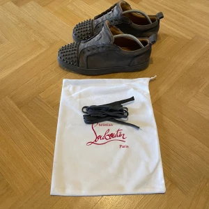 Grå sneakers med nitar från Christian Louboutin - Snygga grå sneakers från Christian Louboutin med nitar och en ikonisk röd sula i storlek 44. Perfekt för en avslappnad stil. Pris kan diskuteras