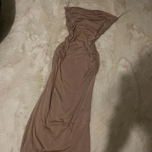 Beige långklänning - Elegant beige långklänning med smala axelband och draperad design. Perfekt för en stilren och sofistikerad look.