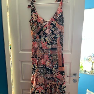 Mönstrad klänning från Odd Molly - Säljer en färgglad klänning från Odd Molly med ett unikt mönster i svart, rosa och orange. Klänningen har en v-ringad hals och knytband. Helt ny! Strl 1 el S. 
