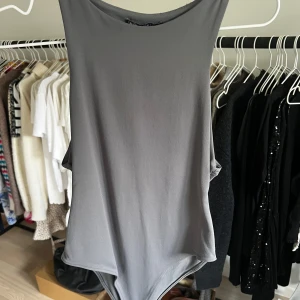 Grå ärmlös bodysuit - Säljer en stilren grå bodysuit med ärmlös design. Perfekt för lager-på-lager eller att bära som den är. Materialet är mjukt och stretchigt för en bekväm passform.