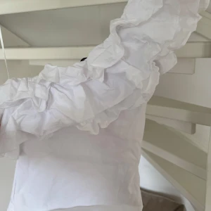 Vit oneshoulder topp med volang från Zara - Säljer en stilren vit oneshoulder topp med volangdetaljer💗 Storlek S/Xs endast använd ett fåtal ggr.