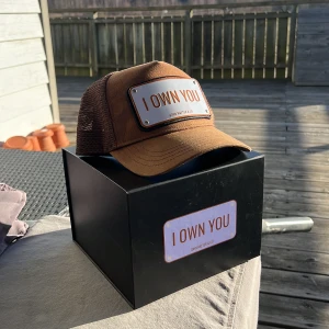 Brun keps från John Hatter & Co - Snygg brun keps från John Hatter & Co med texten 'I OWN YOU' på en metallplatta framtill. Kepsen har ett justerbart spänne baktill för perfekt passform och är tillverkad i ett meshmaterial som ger bra ventilation. Skicket är 7/10, pågrund av att en knapp sitter löst, använd ca 7-8 gånger. Skriv till mig om du har minsta lilla fråga!😌