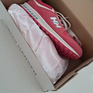 Rosa sneakers från Helly Hansen - Snygga rosa sneakers från Helly Hansen med vit snörning och blå detaljer. Skorna har en rund tå och en mönstrad sula för extra grepp. Perfekta för en sportig look. 