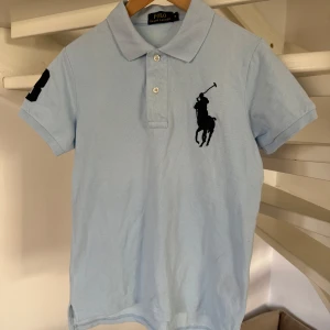 Ljusblå pikétröja från Ralph Lauren storlek S - Säljer min brorsas ljusblå pikétröja från Ralph Lauren med klassisk krage och knappar. Tröjan har en broderad logga på bröstet och en siffra på ärmen. Han kunde ha den när han var runt 171 cm. Endast använd ett fåtal gg