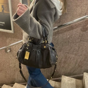 Mörkbrun läder väska från Marc Jacobs - Säljer en snygg mörkbrun skinnväska från Marc Jacobs. Den är vintage och i använt skick. Men är hel förutom en skruv som lossnat. Skriv för fler bilder på väskan då man baka kan ta 5 här. Den är jättefin och cool perfekt som vardags väska. Smutsig innnuti men inget som synd utanpå. Väskan har ”fläckar” där lädret har slitits men inget som är fult. Det blir en mer vintage vibe! Skriv om fler bilder. 34x18x12, väldigt rymig🙌🏻