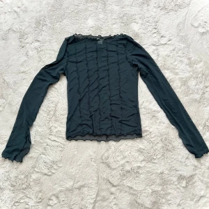 Svart långärmad topp med volangdetaljer - Snygg svart långärmad topp med volangdetaljer längs ärmar och kropp. Perfekt för en stilren look. Tillverkad i ett lätt och bekvämt material.