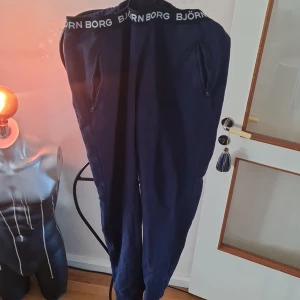 Blå mjukisbyxor från Björn Borg - Säljer ett par bekväma blå mjukisbyxor från Björn Borg. Byxorna har en elastisk midja med Björn Borg-logga och dragkedjor vid fickorna för extra säkerhet. Perfekta för en avslappnad dag hemma eller på språng.