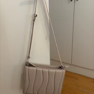 Beige quiltad axelväska - Snygg beige axelväska med quiltad design och justerbar axelrem. Perfekt för att bära dina nödvändigheter med stil. Enkel och elegant för alla tillfällen.