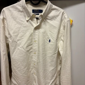 Vit skjorta från Ralph Lauren - Säljer en stilren vit skjorta från Ralph Lauren i storlek L. Skjortan är slim fit och har en klassisk krage med knappar. Den är tillverkad i bomull och har det ikoniska broderade logotypen på bröstet.