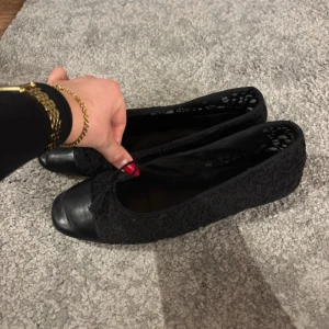 Svarta ballerinaskor med spets från Mango - Snygga svarta ballerinaskor från Mango med spetsdetaljer. Perfekta för en elegant touch till din outfit. Skorna har en rund tå och är tillverkade i ett lätt material för bekväm användning.