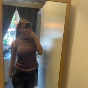 Brun ärmlös topp - Säljer en brun ärmlös topp med ett diskret tryck på bröstet. Perfekt för en avslappnad stil. Passar bra till jeans eller shorts.