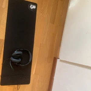 Svarta hörlurar med mikrofon - Säljer ett par svarta hörlurar med vadderade öronkuddar och justerbar bygel. Hörlurarna har en inbyggd mikrofon och en kabelanslutning. Perfekta för gaming eller musiklyssning. Dom funkar till kontroller, man får med musmattan. Knappt använda 