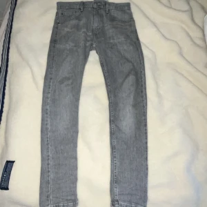Grå jeansbyxor från Levis - Snygga grå jeansbyxor från Levis med klassisk femficksdesign. De har en rak passform och är perfekta för en avslappnad stil. Byxorna har en knappgylf och är tillverkade i slitstarkt denim.