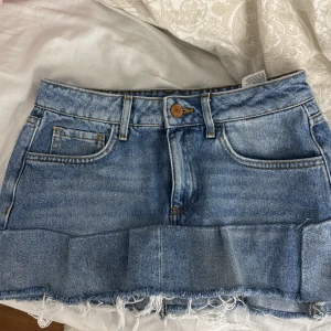 Blå jeanskjol - Snygg blå jeanskjol med klassisk femficksdesign och rå kant. Perfekt för en avslappnad stil. Kjolen har en knapp och dragkedja framtill. Egensydd så vet inte hur bra det håller, säljer då den itne passar mig💕