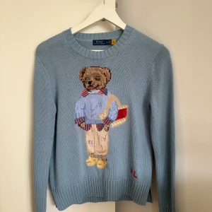 Blå stickad tröja från Polo Ralph Lauren - Säljer en blå stickad tröja från Polo Ralph Lauren med ett broderat motiv av en nalle på framsidan. Har använts några enstaka gånger och har inga skador💕 