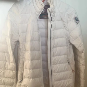 Vit dunjacka från Parajumpers - Säljer en vit dunjacka från Parajumpers. Jackan är superlätt och har en dragkedja framtill. Den är i väldigt bra skick förutom en sminkfläck på vänstra fickan som jag inte fått bort trots flera tvättar. Fortfarande skön, snygg och fullt användbar! Köptes för 3500kr för 2 års sen. Öppen för förhandling