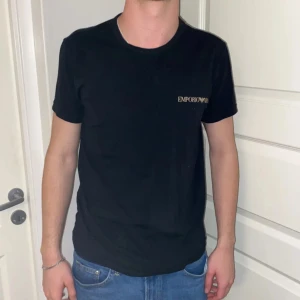 Svart t-shirt från Emporio Armani - Säljer en svart t-shirt från Emporio Armani med diskret logga på bröstet. Klassisk rund halsringning och normal passform. Tillverkad i mjuk bomullsblandning med lite stretch för extra komfort. Han på bilden är 180 cm och väger 62 kg. 