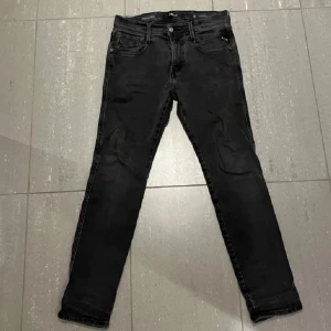 Svarta Replay jeansbyxor Anbass - Svarta jeansbyxor från Replay, modell Anbass. Klassisk femficksdesign med dragkedjegylf och smal passform. Snygga detaljer på bakfickorna och diskret Replay-logga. Perfekta svarta jeans för en stilren look. Storlek W30 L30 