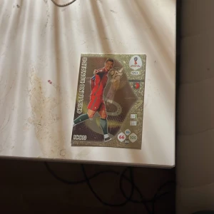 Cristiano Ronaldo fotbollskort ICON - Samlarobjekt: Ett exklusivt fotbollskort med Cristiano Ronaldo i röd matchdräkt. Kortet har holografiska detaljer, FIFA World Cup-logga och spelarstatistik. Perfekt för samlare av sportkort och fotbollsälskare.