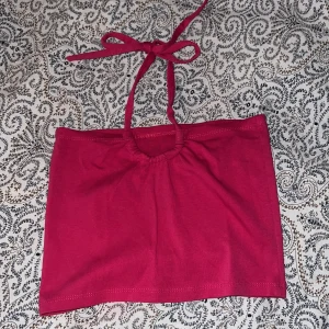 Mörkrosa tubtopp med knytband - Säljer en mörkrosa tubtopp med knytband i nacken. Toppen har en enkel och stilren design med lätt rynkning framtill. 