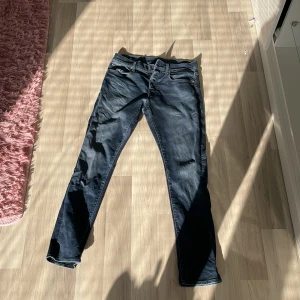 Mörkblå jeansbyxor med knappar - Säljer ett par mörkblå jeansbyxor med klassisk femficksdesign och knäppning med flera knappar framtill av märket Gstar Raw, modell 3301 slim. Byxorna har en smal passform och är perfekta för dig som gillar en stilren look. Storlek W29 L30. Jeansen är ganska använda, men fortfarande i fint och användbart skick. Mitt pris: 269 kr! Hör av er vid minsta fundering 🙌 (kan köpas ihop med de andra gstar jeansen)