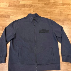 Mörkblå ziptröja från Armani Exchange - Säljer en mörkblå ziptröja från Armani Exchange med hög krage och diskret logga på bröstet. Tröjan har hel dragkedja framtill och två fickor. Perfekt för en stilren och avslappnad look. Passar perfekt som en oversized tröja. Ny pris är 1100 kr, pris kan diskuteras. Nästan helt oanvänd 