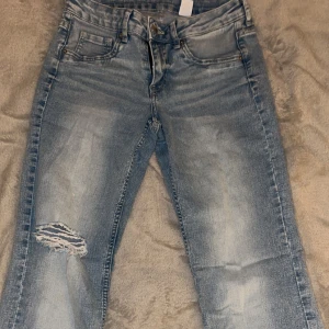 Blåa jeans med hål - Säljer ett par blåa jeans med stretch, samt håll i ena knäet. Köpta ifrån H&M. 
