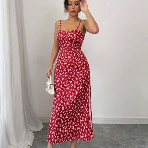 Röd blommig långklänning med smala axelband - Säljer en röd långklänning med vita blommor och smala axelband. Klänningen har en figurnära passform och en liten slits på sidan. Perfekt för sommarens alla tillfällen!