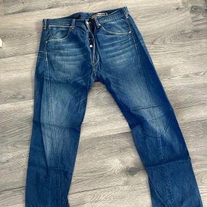 Blå jeansbyxor från Levi's - Klassiska blå jeans från Levi's med fem fickor och knäppning fram. Byxorna har raka ben och tydliga slitningar för en avslappnad look. Perfekta för dig som gillar tidlös denimstil.