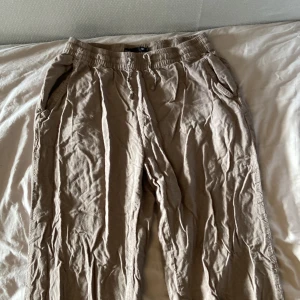 Beiga linnebyxor med resårmidja - Säljer ett par beiga linnebyxor med avslappnad passform och resår i midjan. Byxorna har sidfickor och en bakficka, perfekta för varma dagar. Lätta och luftiga med dragsko i midjan. ca 70 cm i benen 
