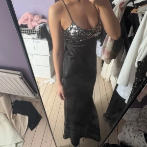 Svart långklänning med paljetter - Säljer en svart långklänning med smala axelband och glittrig paljettbyst. Klänningen har en liten cut-out under bysten och är figurnära upptill. Perfekt för festliga tillfällen när du vill sticka ut. Aldrig använd!