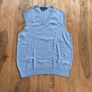 Polo Ralph Lauren – Ljusblå väst i pima cotton - Polo Ralph Lauren – Ljusblå väst i pima cotton  Tunn och mjuk V-ringad slipover i exklusiv pima cotton med gul broderad logga.  Storlek: S (normal i storlek) Färg: Ljusblå med gul logga Material: 100% pima cotton Skick: Mycket fint skick – inga hål eller fläckar Stil: Preppy / Klassisk / Vintage Passform: Rak modell med ribbade kanter Nypris: ca 1 200 kr Pris: 300 kr  Frakt: Skickas snabbt & spårbart