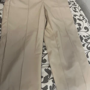 Beiga kostymbyxor från ONLY - Snygga beiga kostymbyxor från ONLY med klassisk passform och raka ben. Byxorna har diskreta fickor bak och stängs med dragkedja och hake framtill. Perfekta för en stilren look.