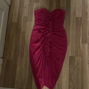 Axelbandslös rosa klänning med volangdetalj - Säljer en snygg axelbandslös rosa klänning med volangdetalj framtill. Klänningen har en tight passform och dragkedja i ryggen. Perfekt för dig som vill sticka ut med en färgstark look!