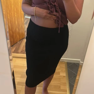 Svart ribbad kjol - Säljer en svart ribbad kjol med kroppsnära passform. Kjolen är midilång och har en stilren look som passar perfekt till olika outfits. Materialet är stretchigt och bekvämt.