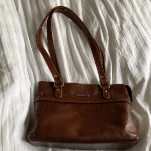 Brun handväska från The Monte - Säljer en klassisk brun handväska i skinn från The Monte. Väskan har dubbla axelband, dragkedja upptill och ett ytterfack med dragkedja på baksidan. Perfekt storlek för det viktigaste och stilren design. 28,5*6,5 cm (botten) 19 cm hög. 400kr