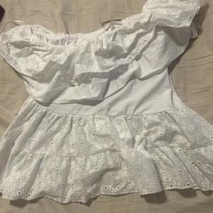 Of shoulder blus från ZARA , aldrig använd, köpt för en vecka sen! Liten i storleken - Söt vit off shoulder blus med volang och broderade blommor. Blusen har en axel och omlottkänsla upptill, samt volanger vid axel.Perfekt för sommarens alla tillfällen!