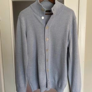 Merino ull kofta från Stenströms - Säljer en stilren ljusblå stickad kofta från Stenströms med ribbad krage och knäppning framtill. Koftan har långa ärmar och bred ribb vid ärmslut och nederkant. Perfekt för lager-på-lager och enkel att matcha.  Nypris: 5000kr 100% merino ull