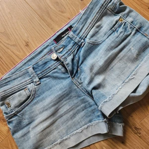 Jeansshorts  - Säljer ett par klassiska blå lågmidjade jeansshorts. Shortsen har knapp- och dragkedjestängning samt detaljer i guld vid fickorna. Perfekta för sommaren! Passar inte mig därför säljer jag 