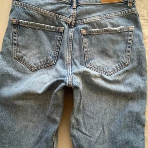 Gina Tricot bootcut jeans med slit  - Ljusblå jeans med klassisk femficksdesign och slitna detaljer på bakfickan. Jeansen är utsvängda med slit från gina. I mycket bra skick